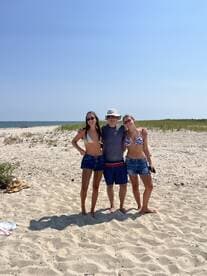 A group of friends poses together on a sunny beach, capturing a moment of fun and relaxation by the water.