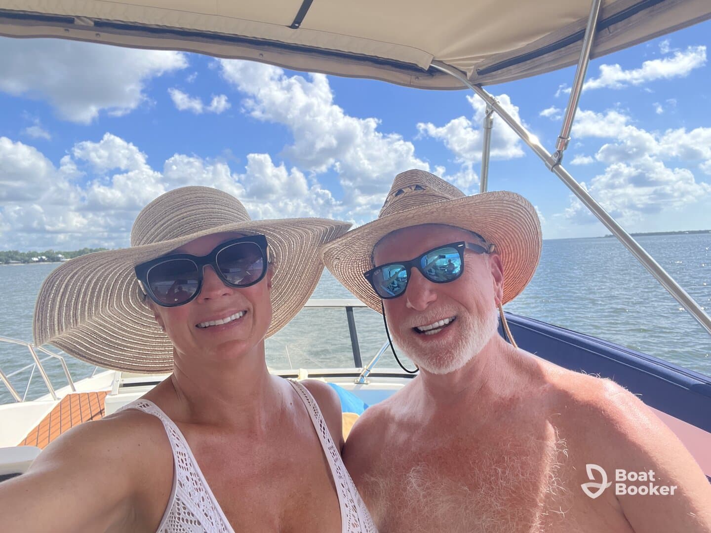 A cheerful couple takes a selfie on a boat under a bright blue sky, enjoying a sunny day on the water.