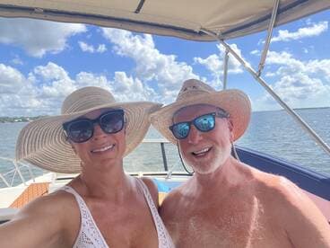 A cheerful couple takes a selfie on a boat under a bright blue sky, enjoying a sunny day on the water.