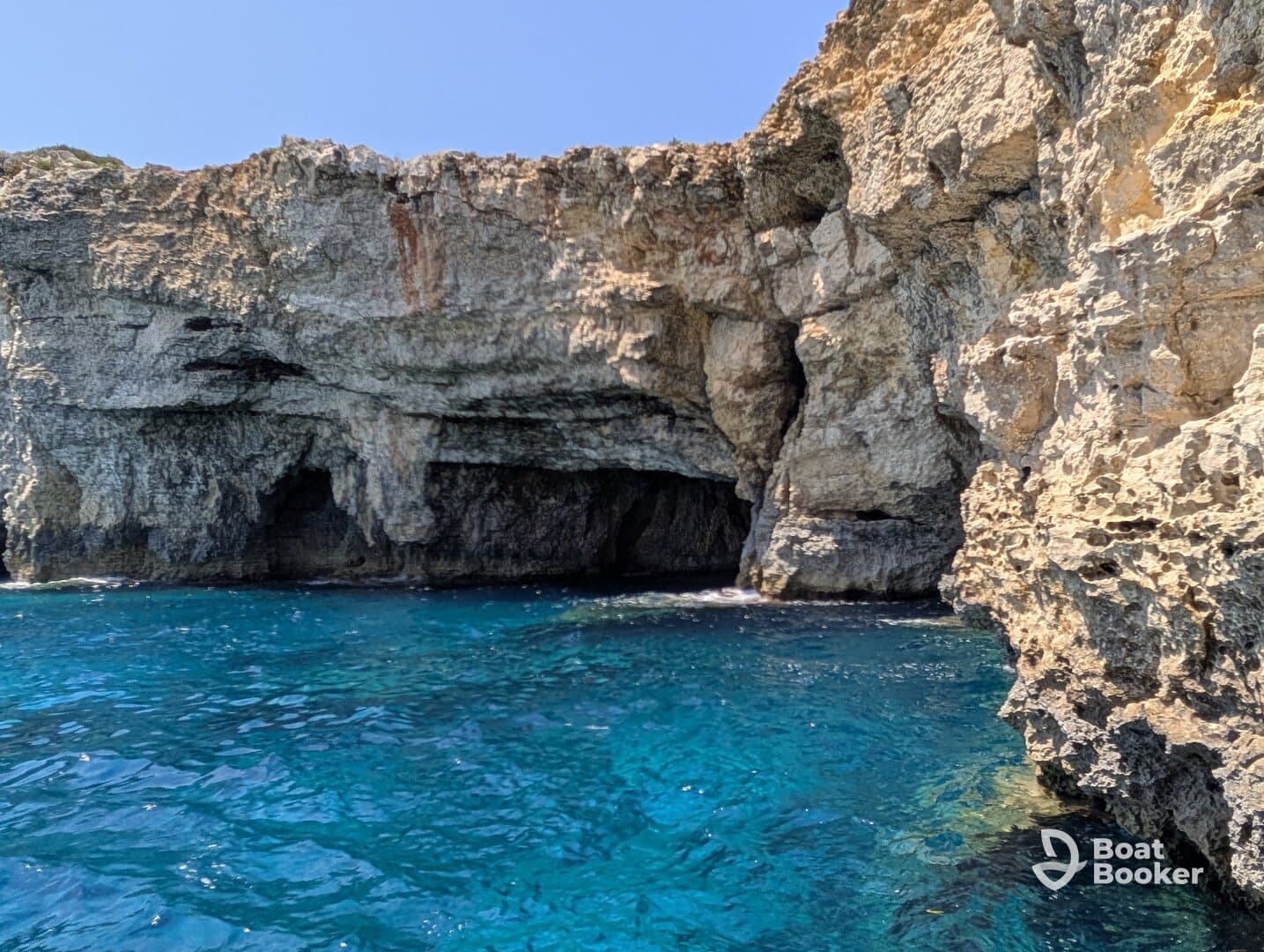 A stunning view of rocky cliffs and a cave along the coastline, showcasing the vibrant blue waters — perfect for exploring natural wonders by boat.