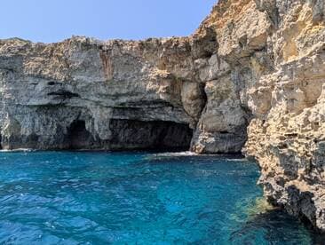 A stunning view of rocky cliffs and a cave along the coastline, showcasing the vibrant blue waters — perfect for exploring natural wonders by boat.