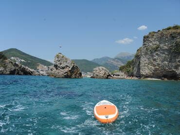 A picturesque view of a coastline with rocky formations and clear turquoise waters, showcasing a paddleboard in the foreground — perfect for water sports enthusiasts and beach lovers.