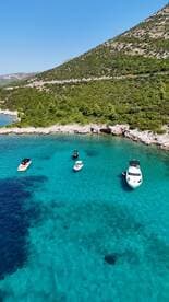 A stunning aerial view of several boats anchored in crystal-clear waters, surrounded by lush greenery — an ideal setting for a relaxing day on the water.