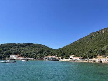 A picturesque view of a serene coastline with lush green hills and charming buildings along the shore, perfect for exploring hidden gems by boat.