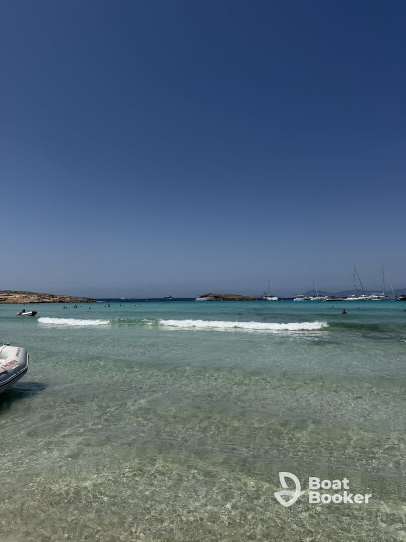 A picturesque beach scene with clear turquoise waters and people enjoying the sun and swimming, perfect for a relaxing day by the sea.