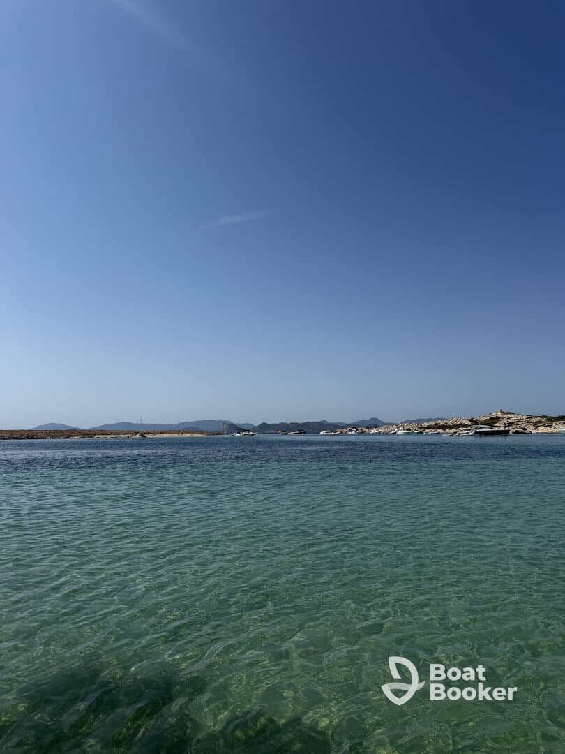 A serene view of a clear turquoise harbor with distant boats and a picturesque coastline, perfect for showcasing the beauty of a day on the water.