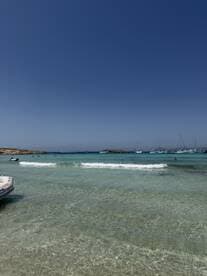 A picturesque beach scene with clear turquoise waters and people enjoying the sun and swimming, perfect for a relaxing day by the sea.