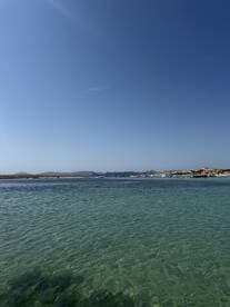 A serene view of a clear turquoise harbor with distant boats and a picturesque coastline, perfect for showcasing the beauty of a day on the water.