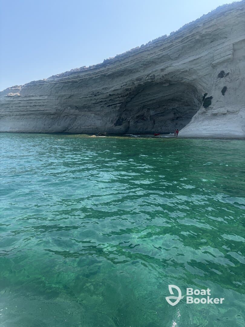 A stunning view of a coastal cave with clear turquoise waters, featuring visitors exploring the area — an ideal destination for adventure seekers and nature lovers.