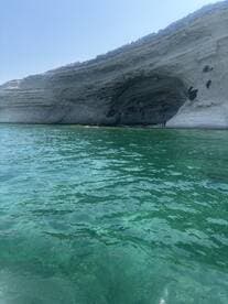 A stunning view of a coastal cave with clear turquoise waters, featuring visitors exploring the area — an ideal destination for adventure seekers and nature lovers.