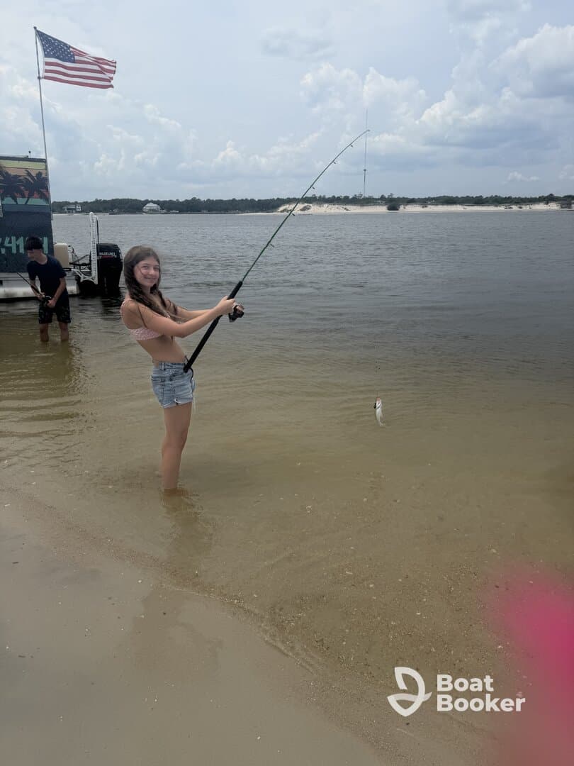 A young girl enjoys a fishing experience in shallow water, showcasing the excitement of catching a fish while having fun outdoors.