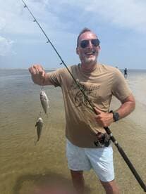A joyful man proudly displays his catch while fishing in shallow waters, showcasing the thrill of outdoor adventures.
