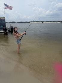 A young girl enjoys a fishing experience in shallow water, showcasing the excitement of catching a fish while having fun outdoors.