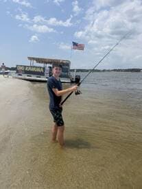 A young boy enjoys fishing in shallow waters near the 'Big Kahuna' tiki boat, capturing the essence of summer fun and outdoor adventure.