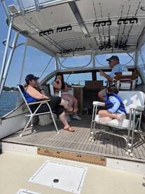 A cozy interior shot of a fishing boat featuring a group of guests, including a child, enjoying their time while discussing fishing plans. The setup highlights the boat's helm and fishing gear, perfect for a day on the water.