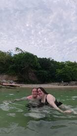 A happy couple enjoys a refreshing swim in tropical waters, surrounded by lush greenery — a perfect moment for beach lovers and adventure seekers.