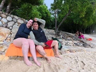 A joyful couple enjoys a relaxing moment on the beach, surrounded by friends — perfect for capturing memorable vacation experiences.