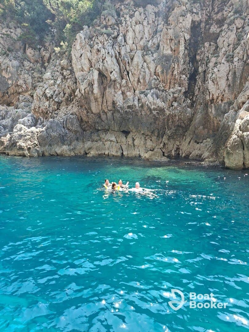 A group of friends enjoys a refreshing swim in the crystal-clear turquoise waters near a rocky coastline, perfect for summer adventures and exploration.