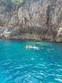 A group of friends enjoys a refreshing swim in the crystal-clear turquoise waters near a rocky coastline, perfect for summer adventures and exploration.