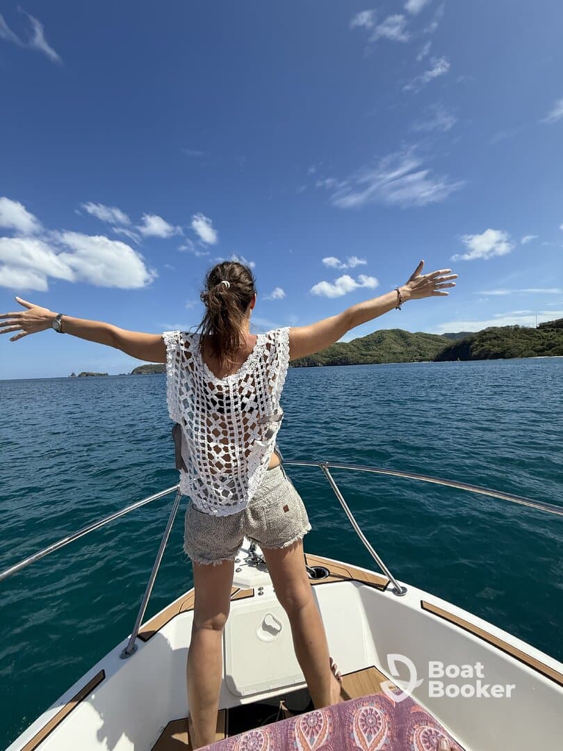 A woman stands on the bow of a boat with arms outstretched, embracing the ocean breeze and sunshine — a perfect moment of freedom on the water.