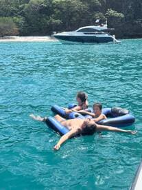 A family enjoys a relaxing day on the water, floating on inflatable loungers while a yacht is anchored nearby — perfect for summer fun and family bonding.