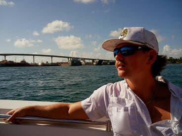 A man enjoys the view from a boat, with a bridge and harbor in the background — a perfect moment capturing the essence of a boating adventure.