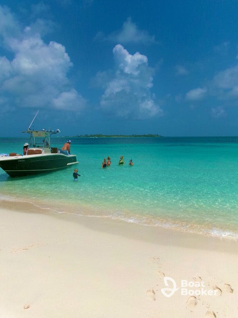 A lively group enjoys a day at the beach, swimming in the crystal-clear turquoise waters with a boat anchored nearby — a perfect scene for summer fun and family adventures.