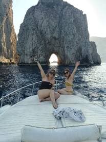Two friends enjoy a fun moment on the bow of a boat near the iconic rock formations of Cabo San Lucas, capturing the essence of a perfect day on the water.