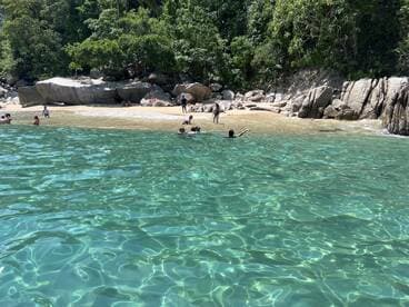 A lively beach scene with people enjoying the clear waters and sandy shore, perfect for a fun day of swimming and relaxation.