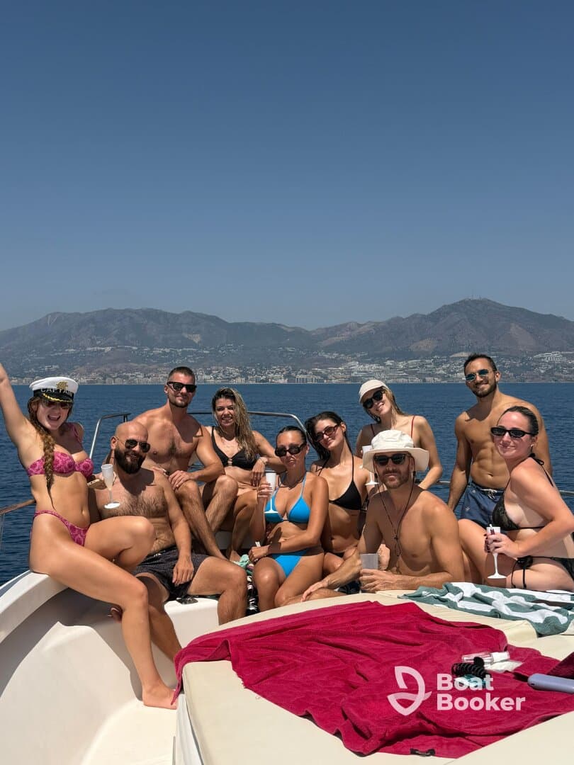 A lively group enjoys a fun day on the water, celebrating with drinks and sunbathing aboard a boat, surrounded by stunning coastal views.