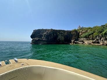 A scenic view from the deck of a boat, showcasing a rocky coastline and a lighthouse in the background — perfect for exploring coastal landscapes.