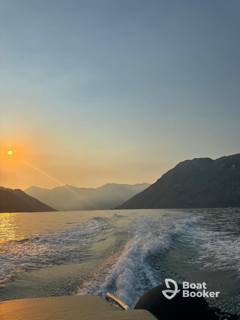 A stunning sunset view from a boat, showcasing the tranquil waters and mountainous backdrop — perfect for serene evening cruises.