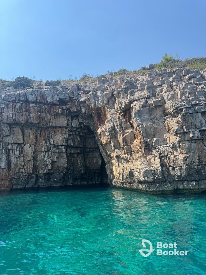 A stunning view of a rocky coastline with a cave entrance, surrounded by crystal-clear turquoise waters — a perfect destination for boat tours and exploration.