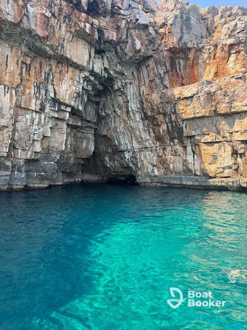 A stunning view of a rocky coastline with a cave entrance, surrounded by crystal-clear turquoise waters — a perfect destination for exploration and adventure.