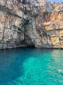 A stunning view of a rocky coastline with a cave entrance, surrounded by crystal-clear turquoise waters — a perfect destination for exploration and adventure.