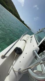 A close-up view of a boat's exterior showcasing its sleek design and features, set against a backdrop of clear turquoise waters and lush greenery.