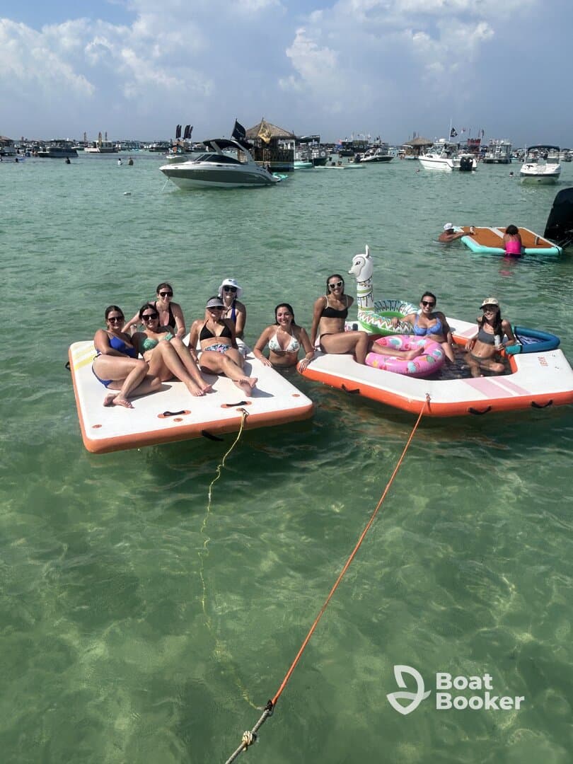 A lively group of friends enjoys a day on the water, relaxing on floating mats and soaking up the sun — the perfect summer party atmosphere.