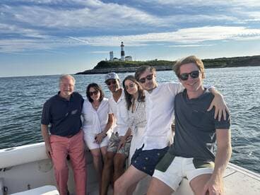 A cheerful group poses together on a boat with a picturesque lighthouse in the background, capturing a memorable moment on the water.