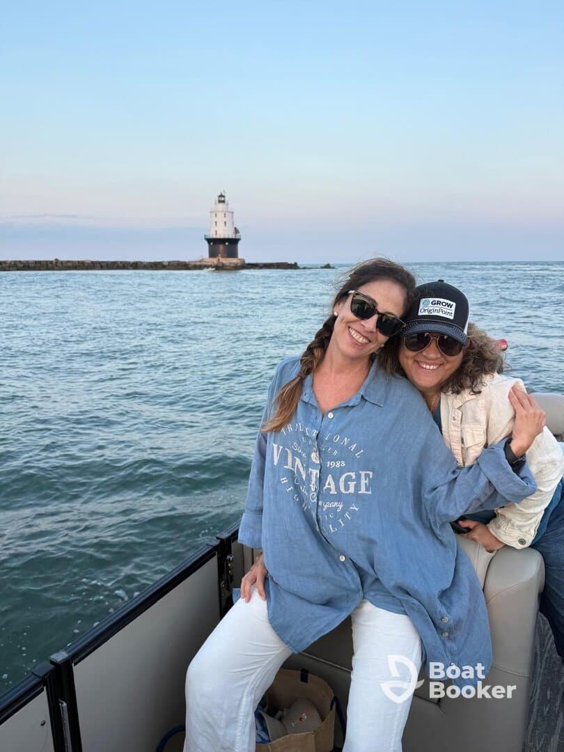 Two friends enjoy a joyful moment on a boat with a picturesque lighthouse in the background, capturing the essence of a fun day on the water.