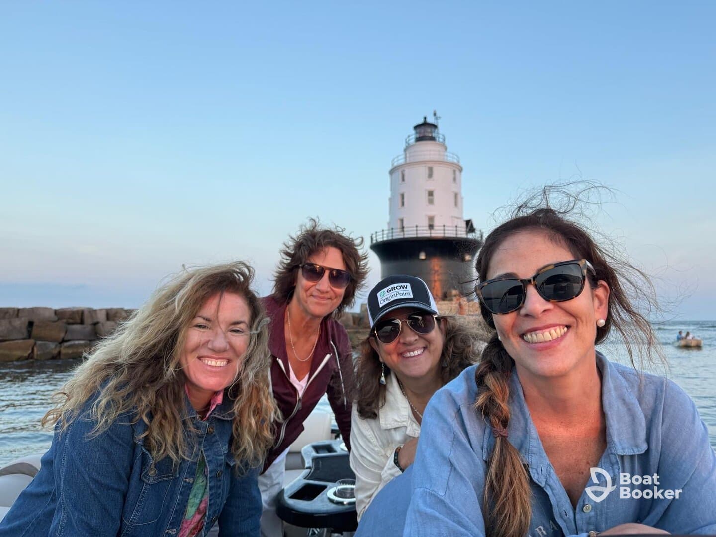 A cheerful group of friends poses for a selfie on a boat with a lighthouse in the background, capturing a memorable moment on the water.