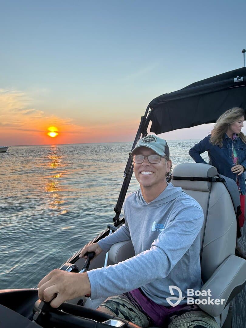 A joyful moment on the water as a young man steers a boat during a stunning sunset, capturing the essence of a perfect boating adventure with friends.