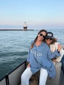 Two friends enjoy a joyful moment on a boat with a picturesque lighthouse in the background, capturing the essence of a fun day on the water.