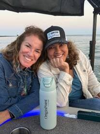 Two friends share a joyful moment on a boat, showcasing their camaraderie against a scenic waterfront backdrop — perfect for memorable outings and celebrations.