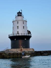A small boat approaches a historic lighthouse, with people onboard enjoying the scenic view — a perfect moment for maritime exploration.