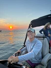 A joyful moment on the water as a young man steers a boat during a stunning sunset, capturing the essence of a perfect boating adventure with friends.
