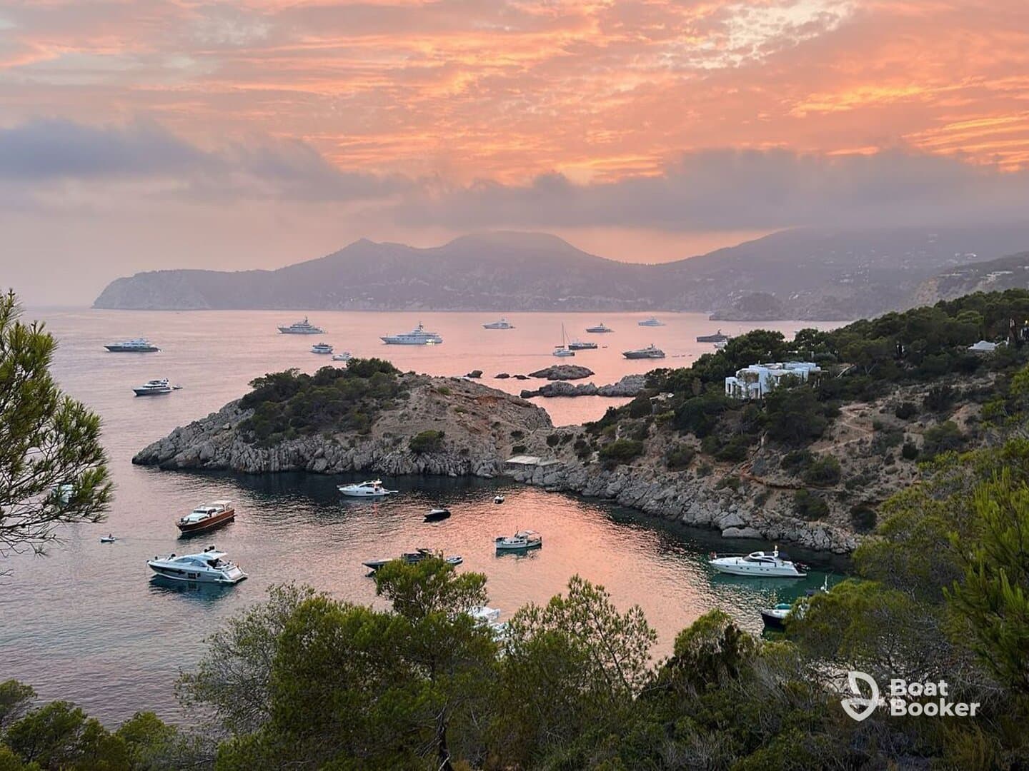 A stunning sunset view over a tranquil harbor filled with various boats, showcasing the beautiful coastline and serene waters — perfect for a peaceful getaway.