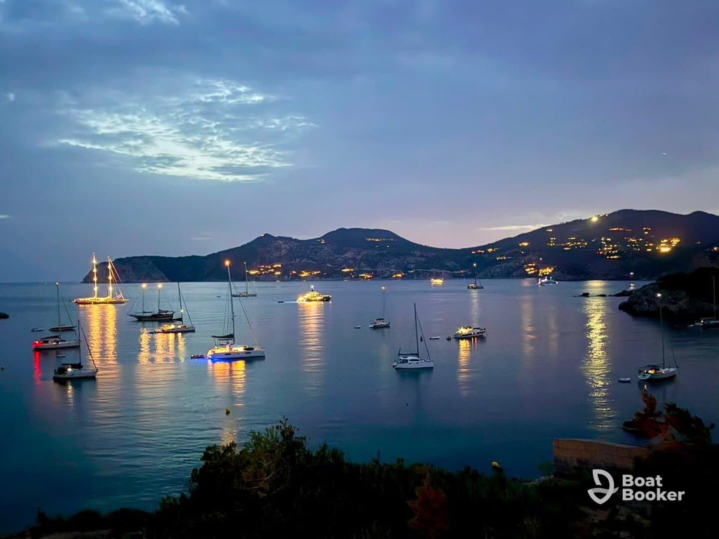 A picturesque harbor scene at dusk, featuring illuminated sailboats reflecting on calm waters — a serene moment perfect for evening boat tours or romantic getaways.