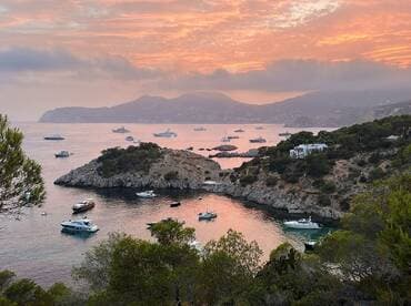 A stunning sunset view over a tranquil harbor filled with various boats, showcasing the beautiful coastline and serene waters — perfect for a peaceful getaway.