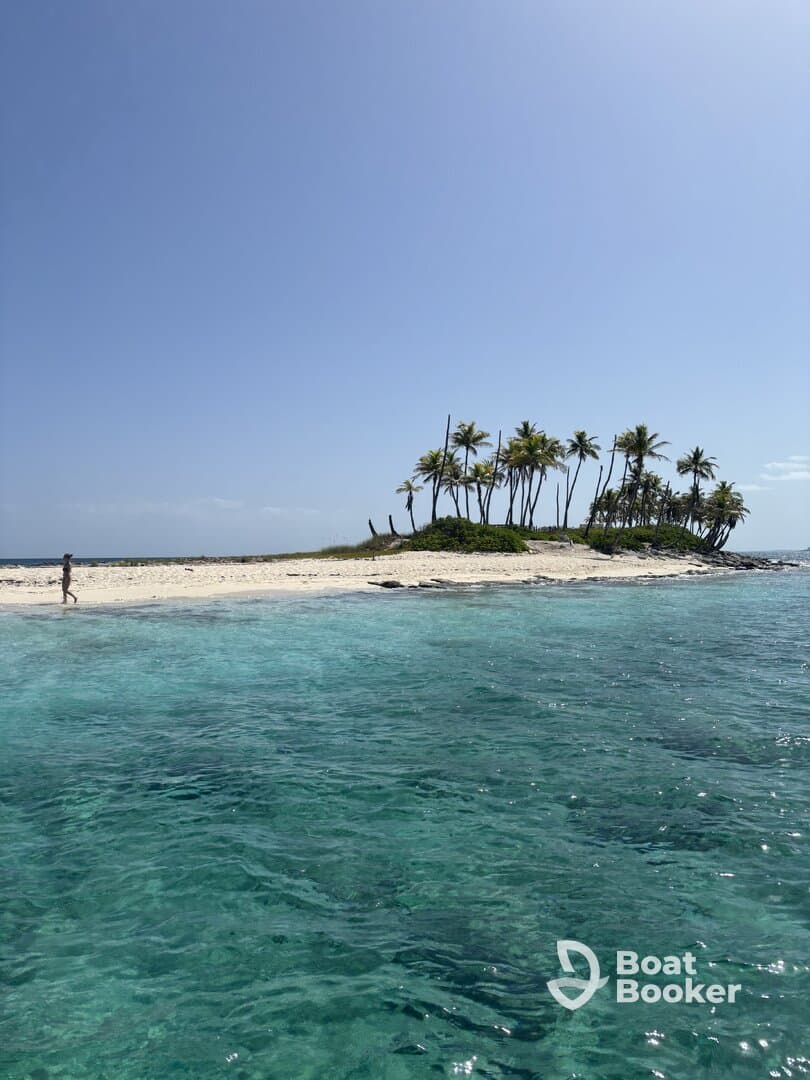 A serene view of a secluded island with a lone figure walking along the sandy beach, surrounded by crystal-clear waters — a perfect tropical getaway.