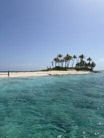 A serene view of a secluded island with a lone figure walking along the sandy beach, surrounded by crystal-clear waters — a perfect tropical getaway.